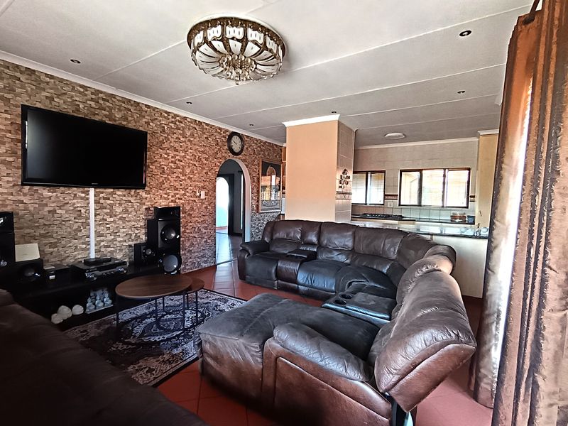 Spacious open-plan living area featuring a stone veneer accent wall, tiled flooring, and a seamless transition into the adjacent kitchen space.
