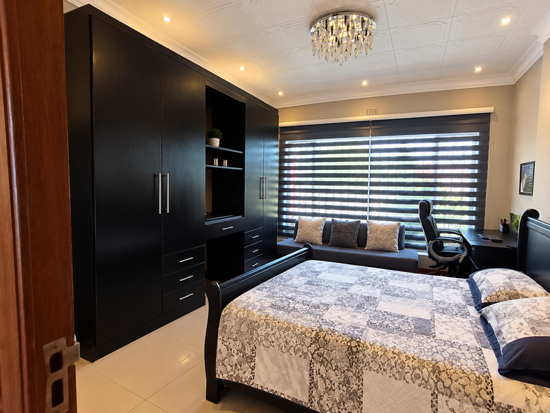 A well-maintained bedroom featuring extensive built-in black cabinetry, tiled flooring, decorative ceiling details, and modern roller blinds for privacy.