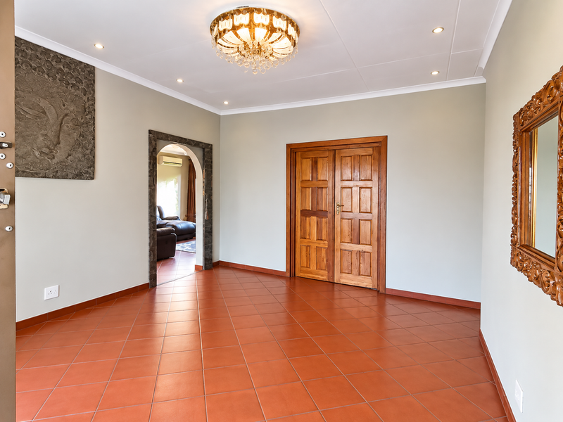 Spacious entrance hall featuring terracotta-style floor tiles, a decorative chandelier, and elegant double wooden doors leading to adjacent living areas.