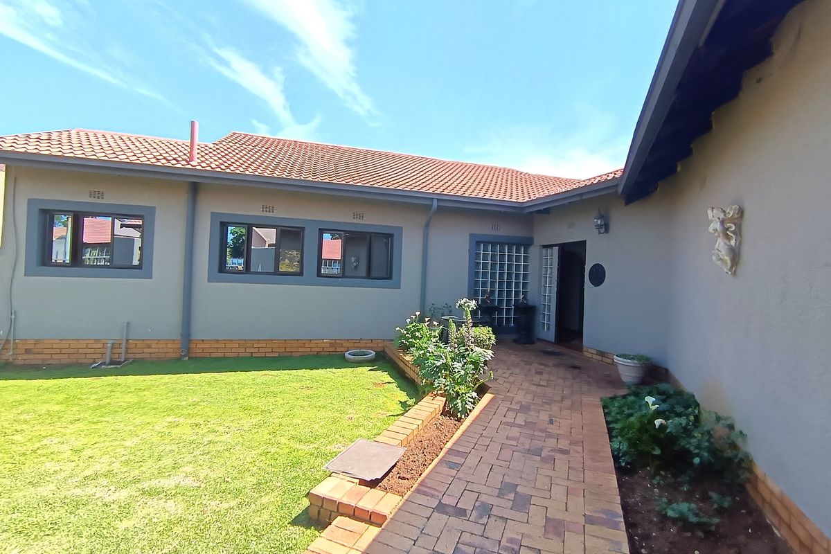 A well-maintained rear exterior view featuring a brick paved walkway, landscaped garden area, and tiled roof structure.