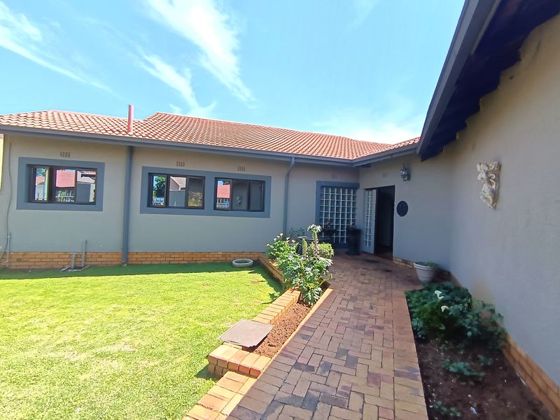 A well-maintained rear exterior view featuring a brick paved walkway, landscaped garden area, and tiled roof structure.