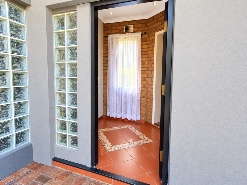 A bright and welcoming entrance hall featuring a unique glass block wall, exposed brick accents, and decorative tiled flooring.