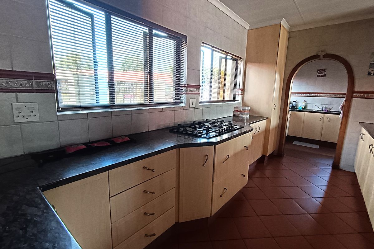 A functional kitchen featuring light wood cabinetry, dark laminate countertops, a gas hob, and tiled flooring, with an arched opening leading to an adjacent area.