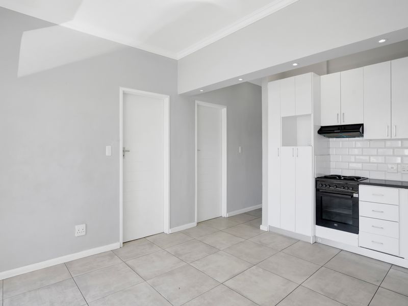 Modern kitchen featuring white cabinetry, subway tile backsplash, built-in oven with gas hob, extractor fan, and neutral tiled flooring.