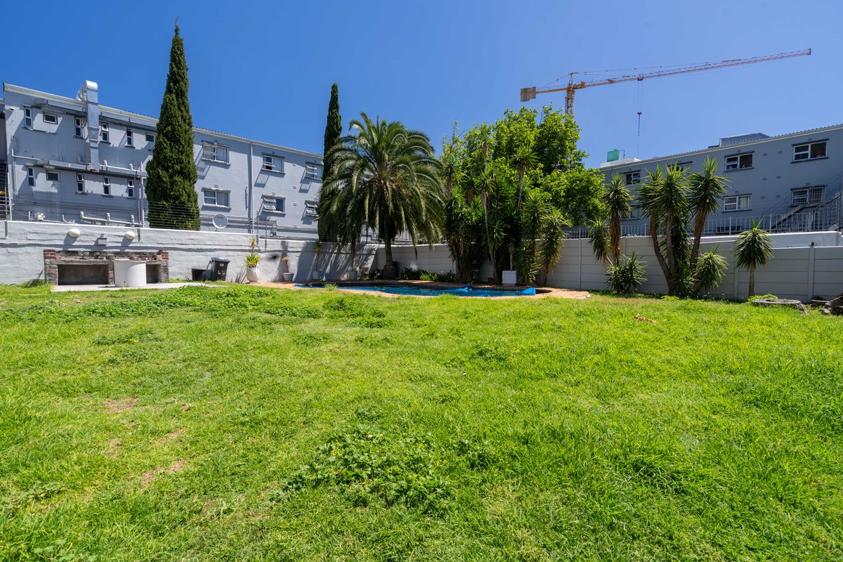 Rear garden area featuring a swimming pool, built-in braai, and perimeter boundary wall, set against a backdrop of apartment buildings.