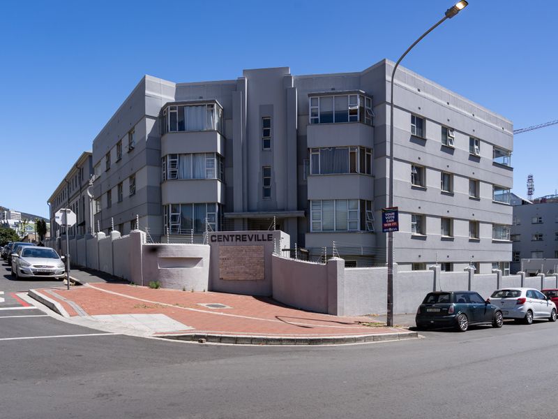 Street-level view of the Centreville apartment building, featuring a multi-story grey facade, perimeter wall with electric fencing, and paved sidewalk access.