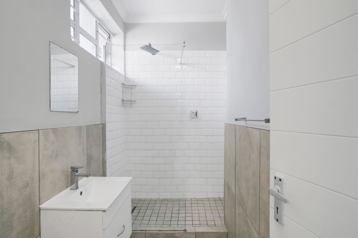 A clean, modern bathroom featuring a walk-in shower with white subway tiles, a vanity basin, and neutral floor tiling.