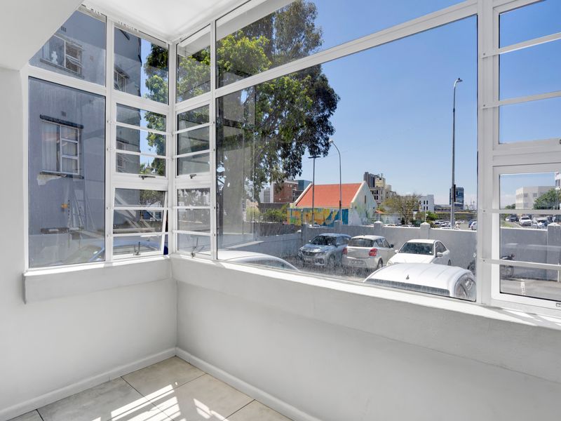 An enclosed balcony or sunroom featuring large windows, tiled flooring, and views of the surrounding urban area.