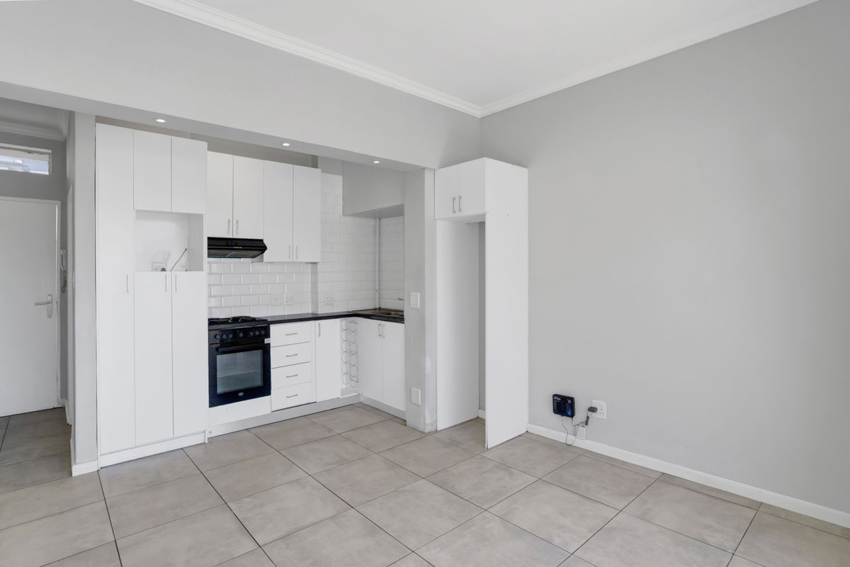 A clean, modern kitchen featuring white cabinetry, subway tile backsplash, built-in oven and hob, and neutral tiled flooring in an open-plan layout.