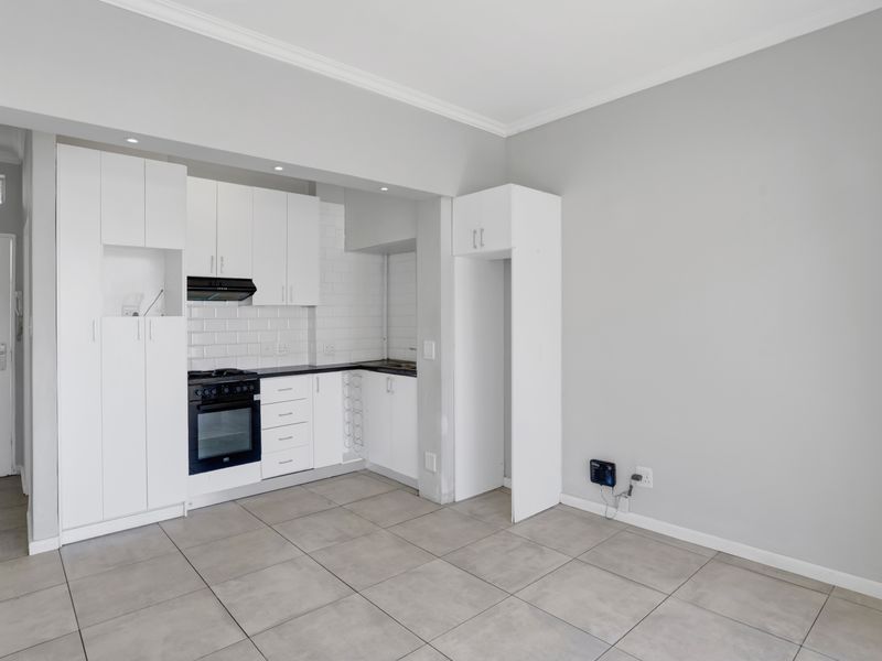 A clean, modern kitchen featuring white cabinetry, subway tile backsplash, built-in oven and hob, and neutral tiled flooring in an open-plan layout.