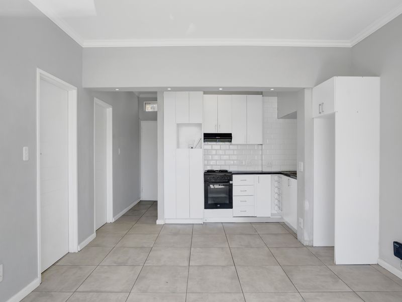 A clean, modern kitchen featuring white cabinetry, subway tile backsplash, built-in oven, and neutral ceramic floor tiles in an open-plan layout.