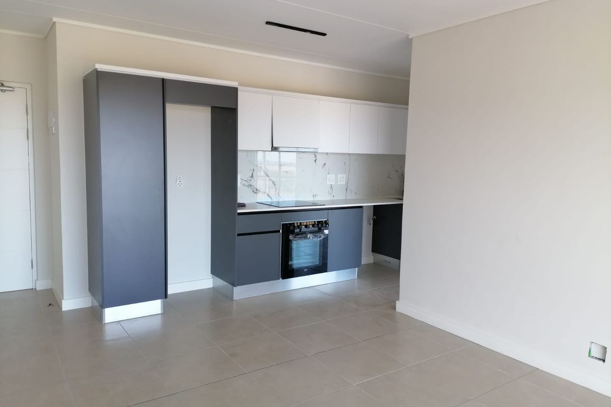 Modern, empty kitchen featuring sleek two-tone cabinetry, built-in oven, electric hob, extractor fan, and elegant marble-look splashback with neutral tiled flooring.