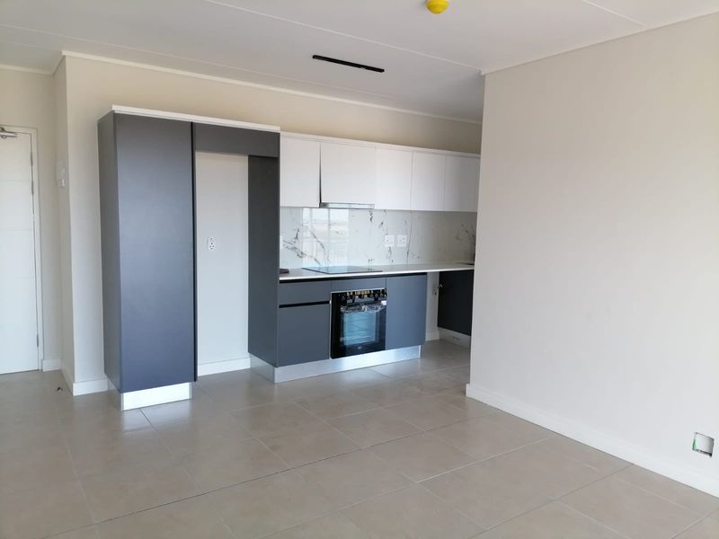 Modern, empty kitchen featuring sleek two-tone cabinetry, built-in oven, electric hob, extractor fan, and elegant marble-look splashback with neutral tiled flooring.