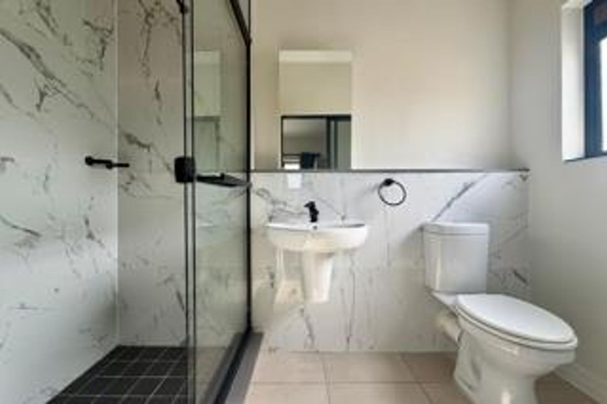 Modern bathroom featuring a glass-enclosed shower, pedestal sink, toilet, and elegant marble-look wall tiling with contemporary black fixtures.