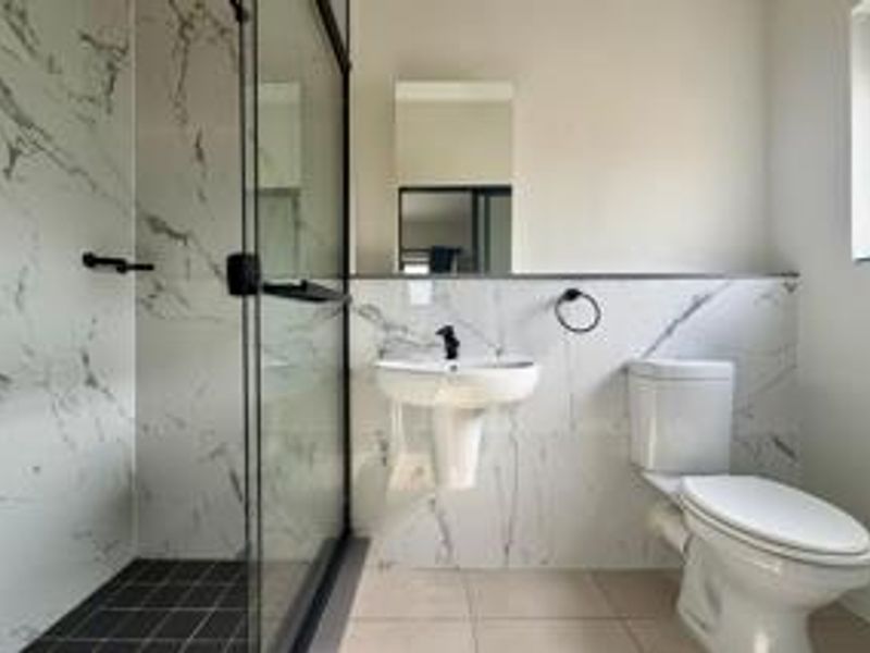 Modern bathroom featuring a glass-enclosed shower, pedestal sink, toilet, and elegant marble-look wall tiling with contemporary black fixtures.