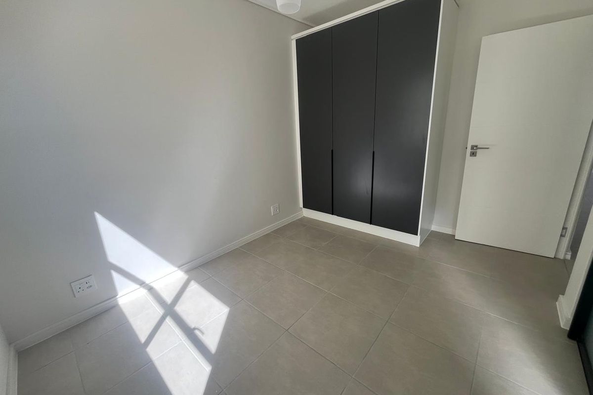 A bright, empty bedroom featuring modern grey tiled flooring and a sleek, dark-toned built-in wardrobe.