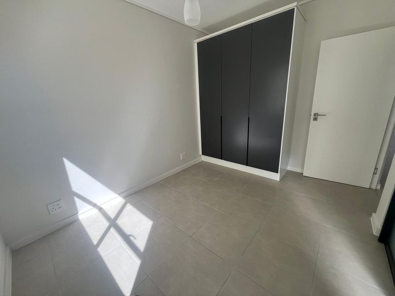 A bright, empty bedroom featuring modern grey tiled flooring and a sleek, dark-toned built-in wardrobe.
