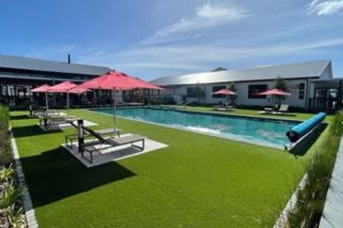 A well-maintained outdoor swimming pool area featuring artificial turf, paved surrounds, and modern building structures in the background.