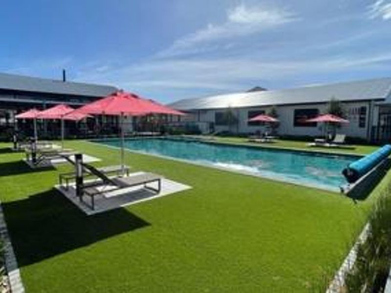 A well-maintained outdoor swimming pool area featuring artificial turf, paved surrounds, and modern building structures in the background.