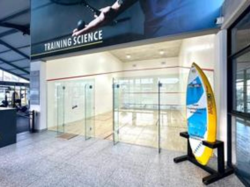 A well-maintained indoor squash court featuring glass walls and professional timber flooring within a modern sports facility.