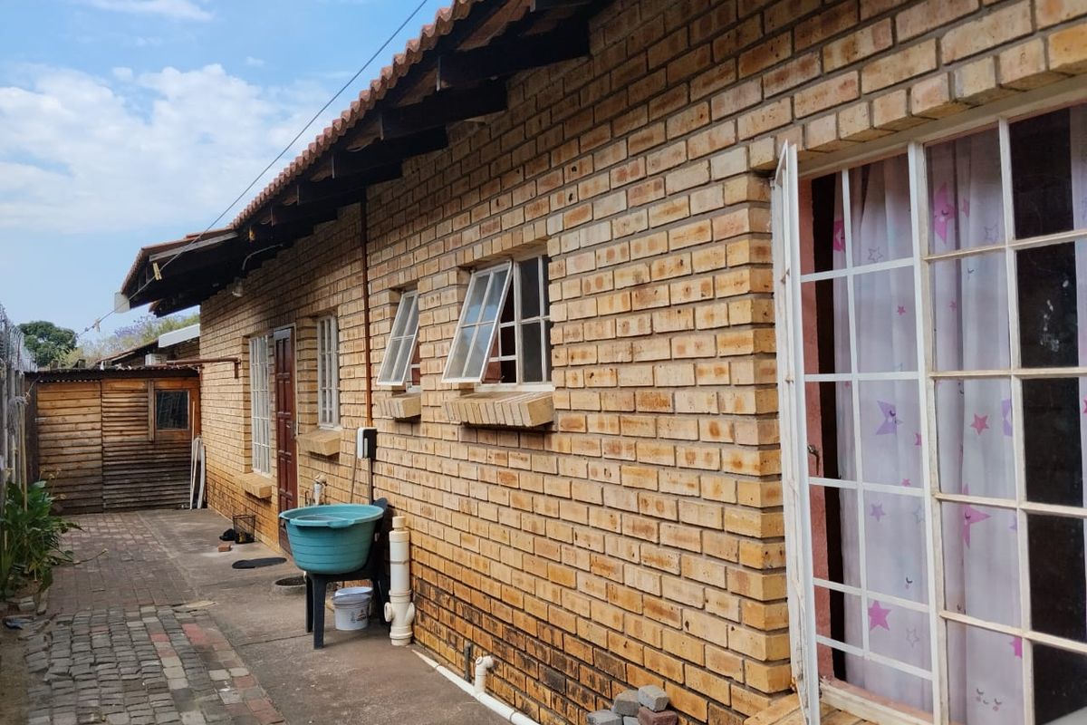 A side view of the house featuring face brick exterior walls, tiled roofing with exposed rafters, and paved pathways along the building perimeter.
