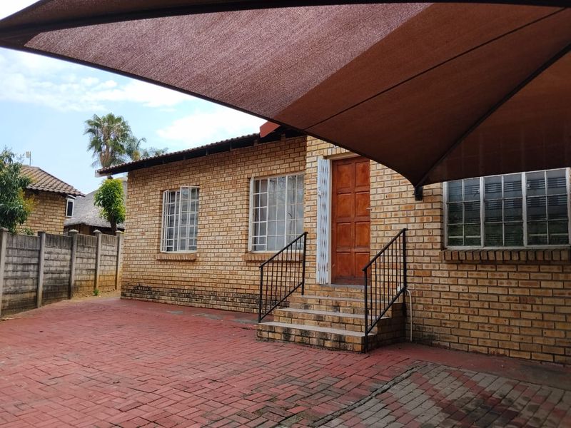 Front exterior view of a face brick house featuring a paved driveway, concrete entrance steps with metal railings, and a large overhead shade sail.