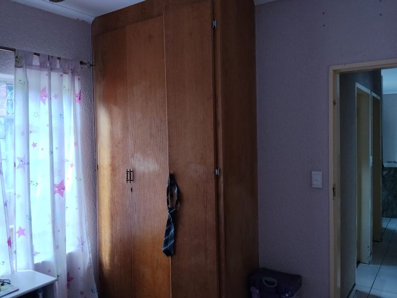 A bedroom featuring a built-in wooden wardrobe with visible wear, requiring cosmetic updates to improve the overall aesthetic and condition of the space.