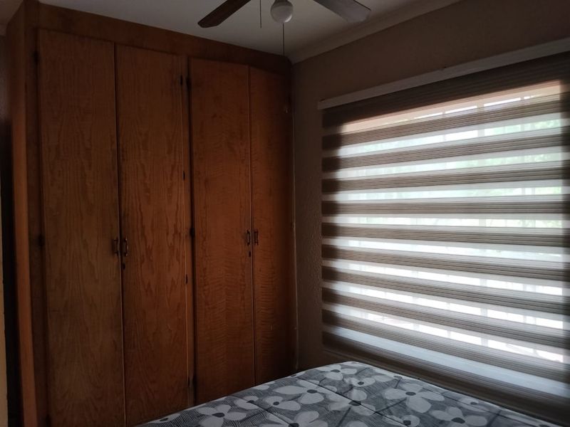 A bedroom featuring a large built-in wooden wardrobe, a ceiling fan, and modern dual-layer roller blinds for adjustable light control.