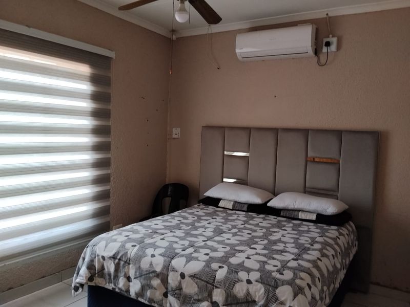 A bedroom featuring a split-system air conditioner, ceiling fan, and roller blinds, with tiled flooring throughout.