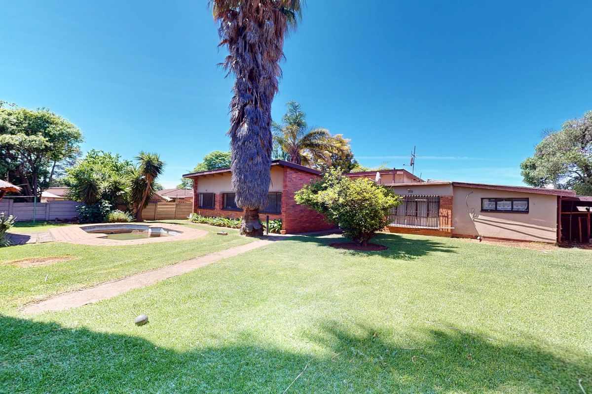Rear view of the property featuring a brick facade, a swimming pool, a large lawn, and a thatched gazebo in the garden.