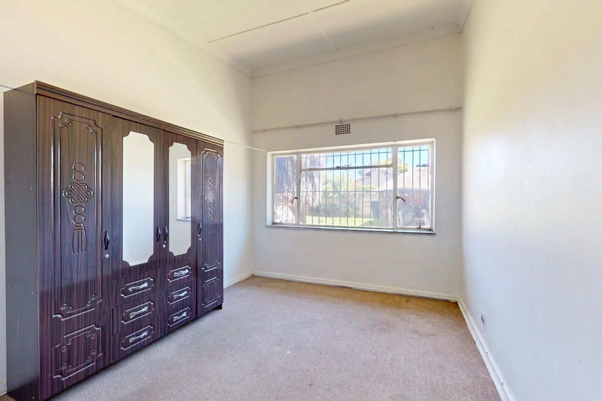 A bedroom featuring carpet flooring, security bars on the window, and ceiling tiles. The space is ready for a modern update.