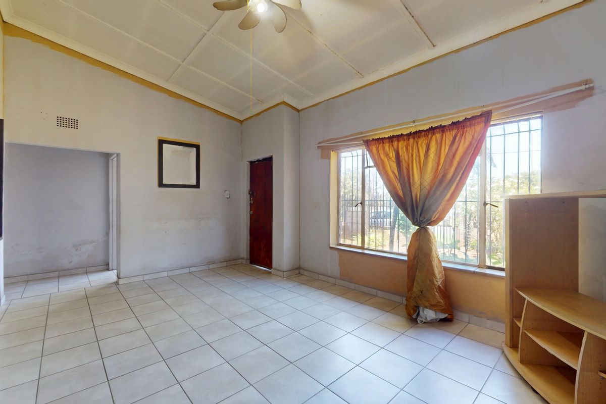 A spacious, empty living area featuring tiled flooring, a ceiling fan, and large windows with security bars, ready for a modern update.