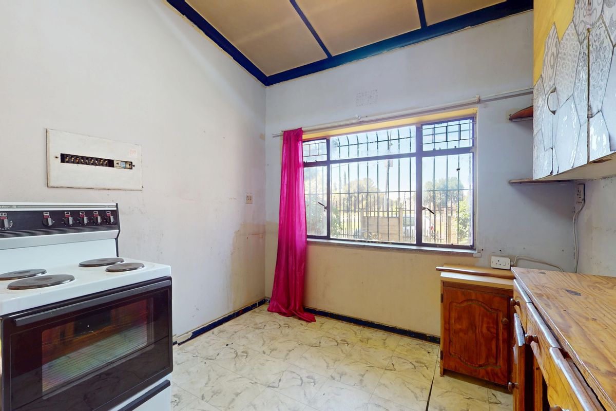 A dated kitchen featuring a freestanding stove, basic cabinetry, and tiled flooring, requiring significant renovation and cosmetic updates to improve its condition.