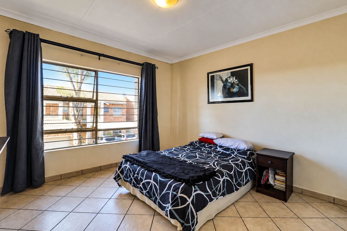 A well-lit bedroom featuring tiled flooring, a large window with security bars, and neutral wall finishes.