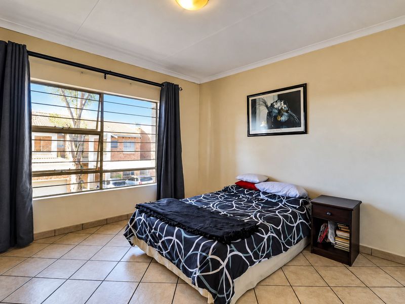 A well-lit bedroom featuring tiled flooring, a large window with security bars, and neutral wall finishes.
