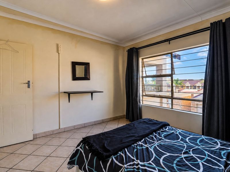 A bedroom featuring tiled flooring, coved ceilings, and a window with security bars. The room shows signs of wall discoloration and water staining.