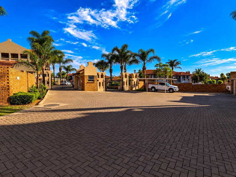 A well-maintained apartment complex entrance featuring brick paving, secure gated access, and covered parking bays.
