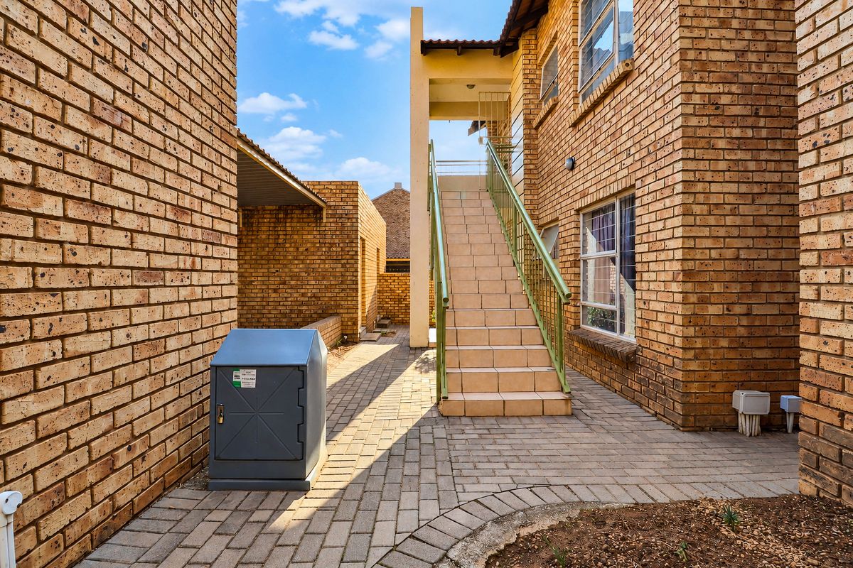 Exterior view of an apartment complex featuring face brick construction, a paved walkway, and an external staircase with metal balustrades leading to upper levels.