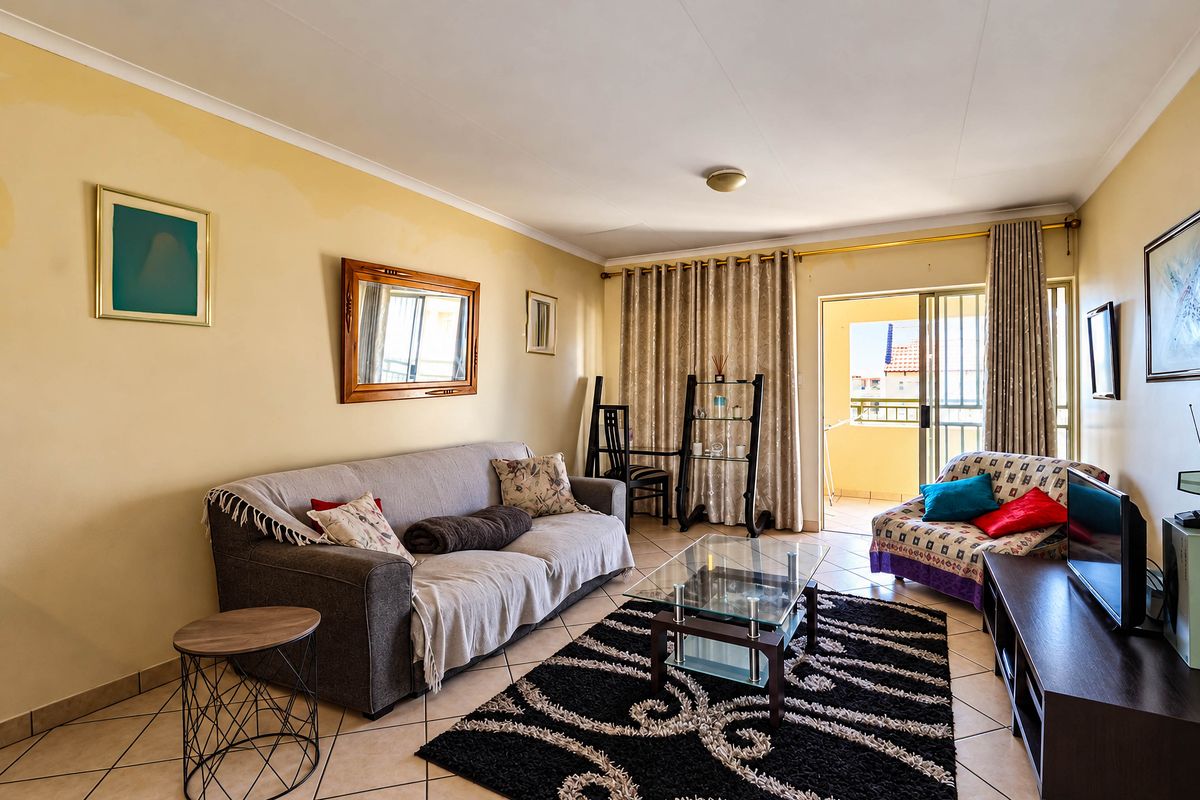 A living room featuring tiled flooring and a sliding glass door leading to a balcony, with neutral wall tones and coved ceiling details.