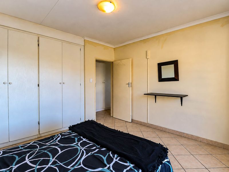 A bedroom featuring tiled flooring, built-in cupboards, and an internal door, showing signs of wall discoloration and water staining.