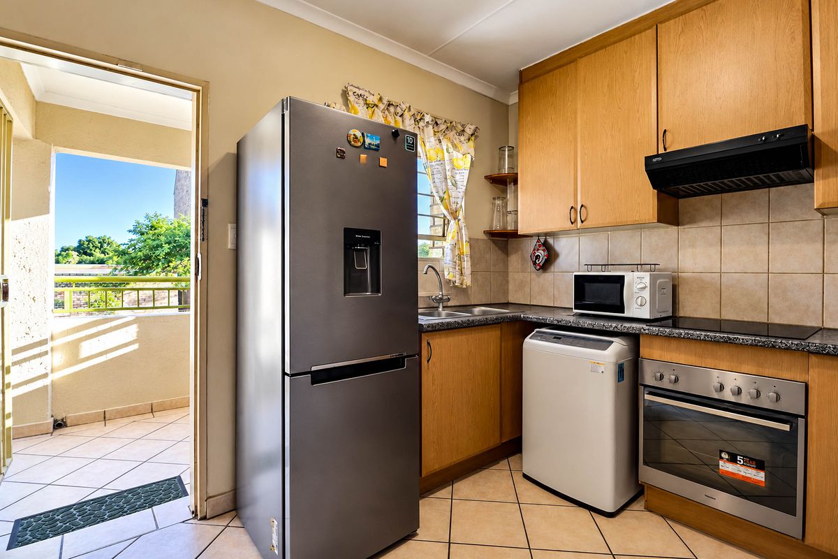 A functional kitchen featuring light wood cabinetry, granite-look laminate countertops, a built-in oven with extractor fan, and direct access to an outdoor balcony area.