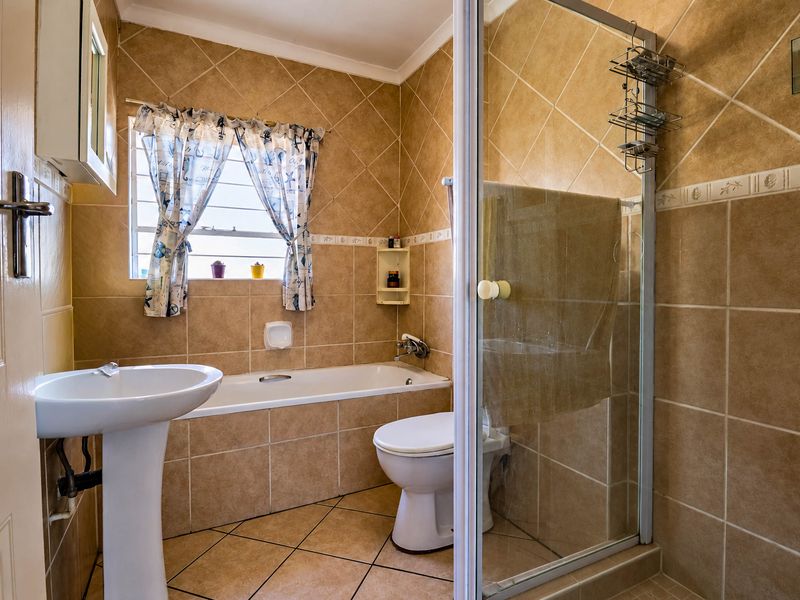 A functional bathroom featuring a pedestal basin, a built-in bathtub, and a separate shower enclosure with full-height ceramic tiling.