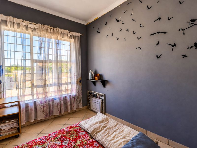 A bedroom featuring tiled flooring and a window with security bars, finished with grey walls and decorative wall decals.