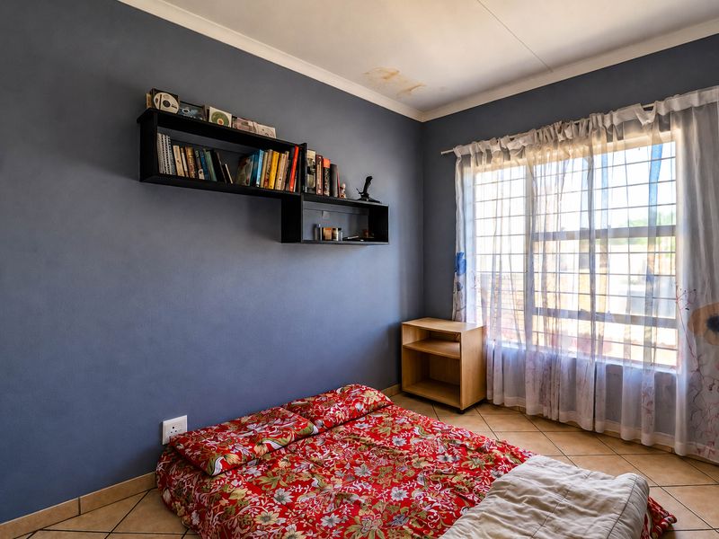 A bedroom featuring tiled flooring, security bars on the window, and built-in wall shelving, with a visible water stain on the ceiling.