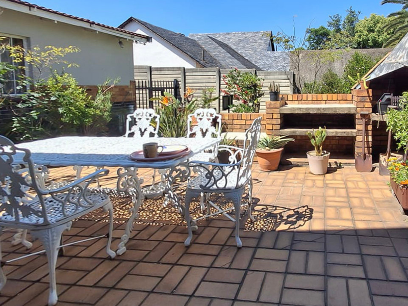 A paved outdoor patio area featuring a built-in brick braai and established garden surroundings, ideal for outdoor entertaining.