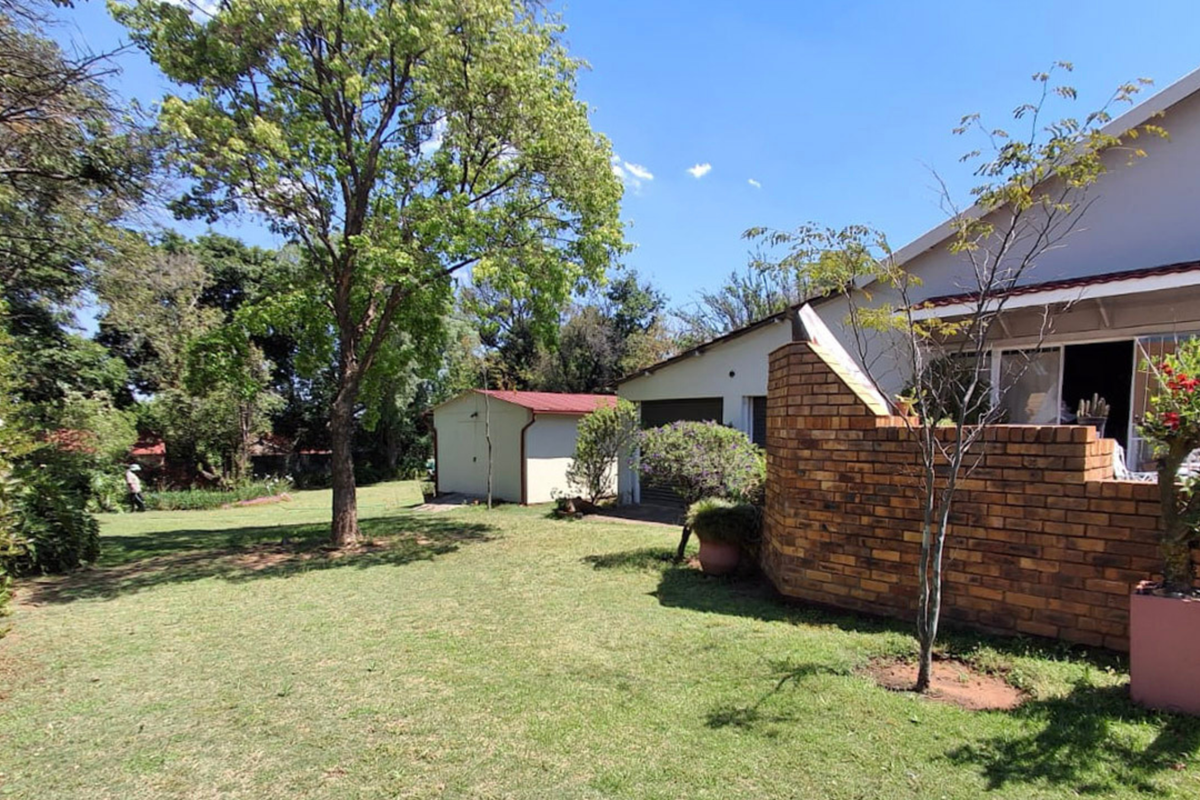 A spacious rear garden featuring a well-maintained lawn, a brick boundary wall, and a detached outbuilding under a tiled roof.