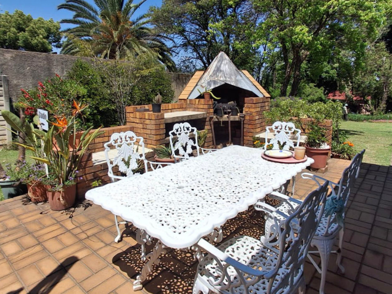 Outdoor patio area featuring a brick built-in braai and paved flooring, set within a landscaped garden environment.