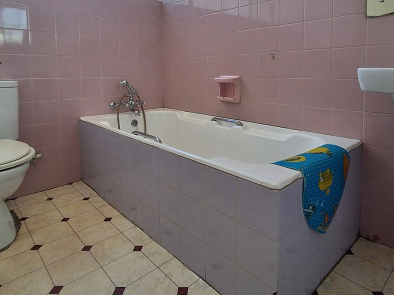 A dated bathroom featuring pink wall tiles, a built-in bathtub, a pedestal sink, and a standard toilet.