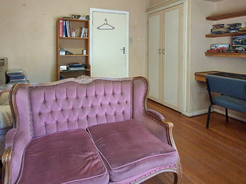 A bedroom featuring hardwood flooring, built-in cupboards, a built-in desk, and wall-mounted shelving, requiring cosmetic updates to the wall finishes.