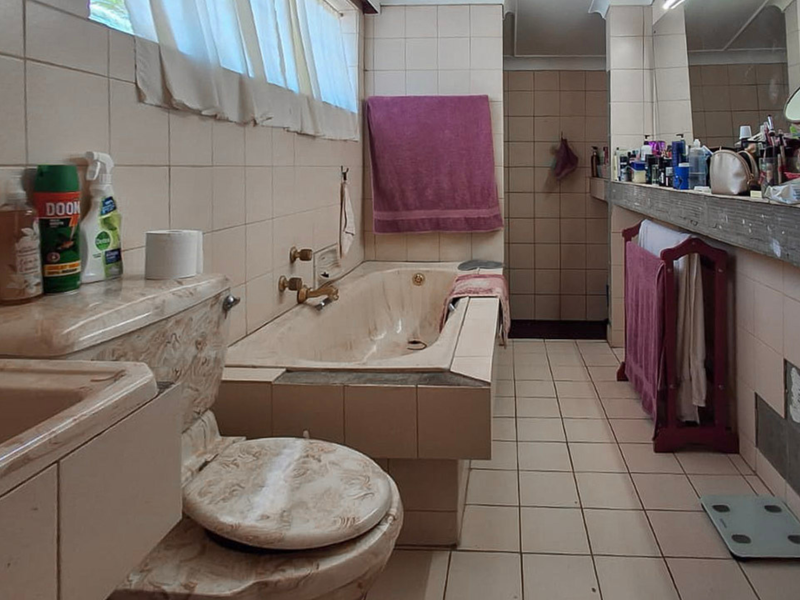 A dated bathroom featuring a built-in bathtub, tiled surfaces, and a vanity area, currently requiring cosmetic updates and repairs to the wall tiling.